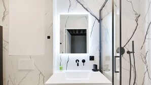 Ein Badezimmer mit einem weißen Marmorwaschbecken, einem Spiegel, einer Dusche und einem Handtuchhalter.