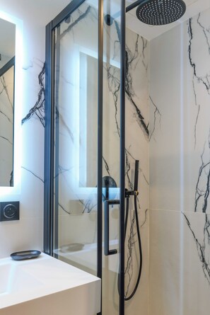 Un baño moderno con ducha de vidrio, paredes de mármol y lavamanos blanco.