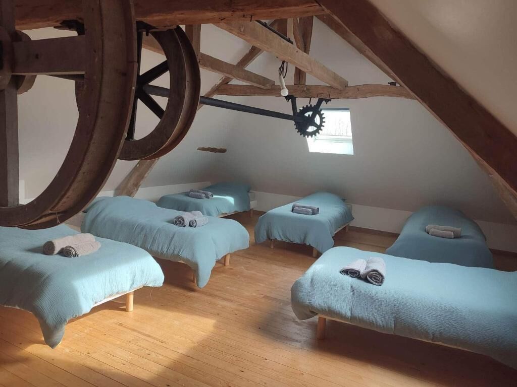 Quarto com quatro camas dispostas em semicírculo, vigas de madeira e uma grande estrutura circular de madeira.