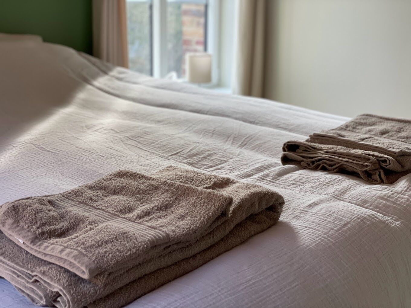 Un lit bien fait, avec des serviettes pliées, et une fenêtre avec des rideaux.