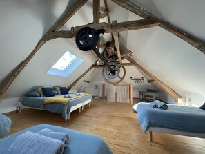 A cozy attic bedroom with a sloped ceiling, wooden beams, a skylight, two beds, and a small table. - Le Gite du Moulin de la Pisciculture Situé Dans la Vallée de la Canche (Monchel-sur-Canche)