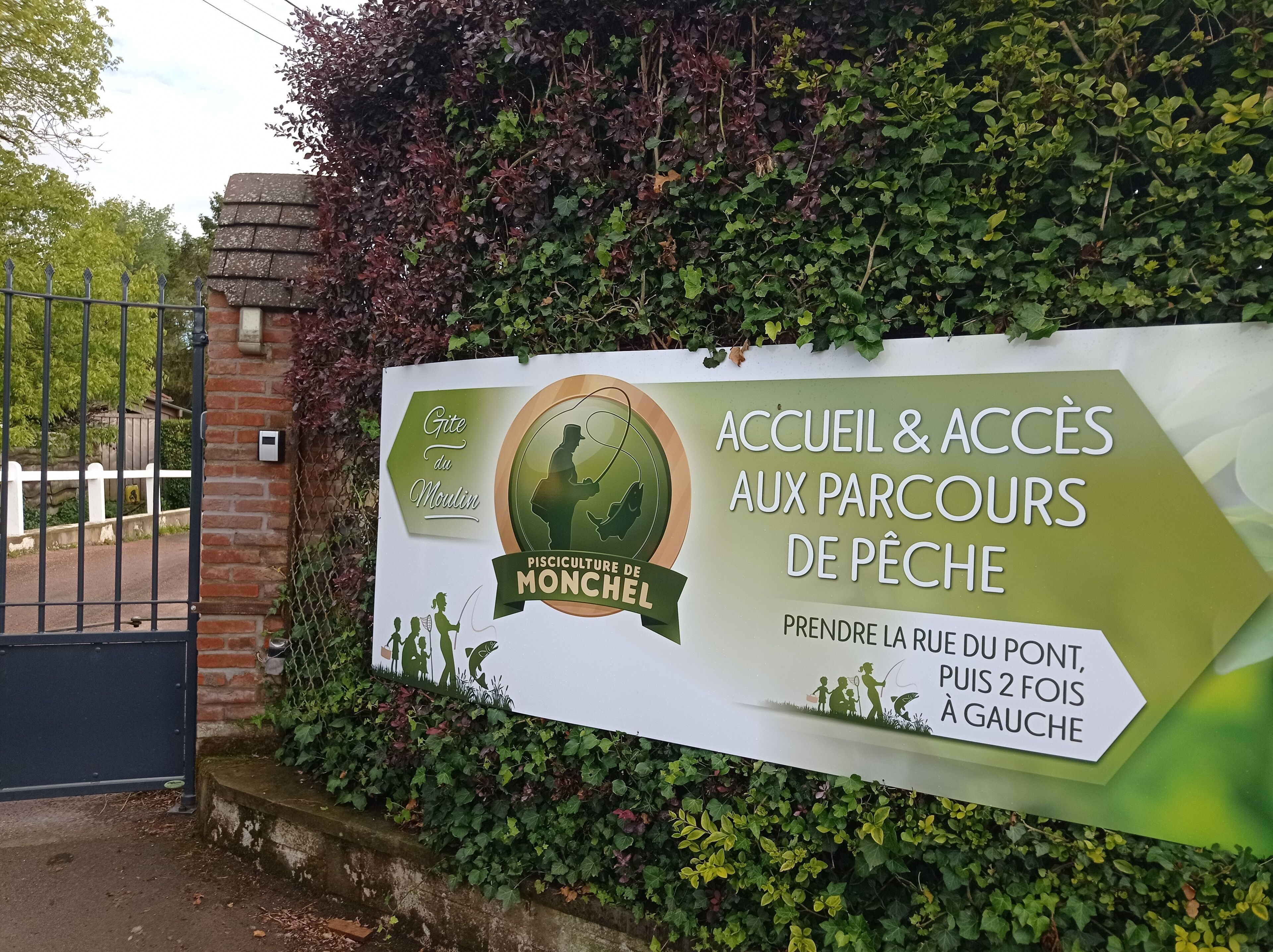 A sign for a fishing park entrance with a gate and greenery.