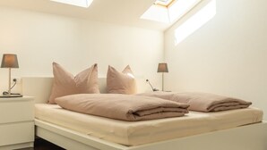 Une chambre moderne avec une lucarne, un lit avec une literie beige, deux tables de chevet avec des lampes et un plancher en bois foncé.