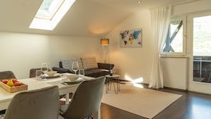 Un coin repas avec une table dressée pour deux personnes, un canapé et une petite table d’appoint sur laquelle se trouvent une bouteille et des verres.