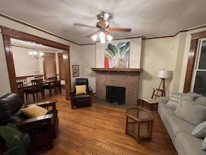 A living room with hardwood flooring, a fireplace, a ceiling fan, and a dining area with wooden furniture.