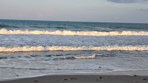 A beach with waves, a boat in the distance, and a cloudy sky. - Historical NASA Home (Cape Canaveral)