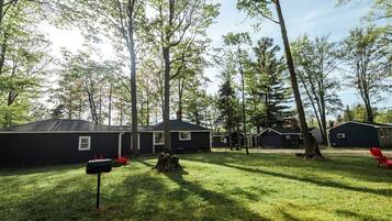 Un terrain de camping doté de plusieurs cabanes, d’une pelouse bien entretenue et d’une grande souche d’arbre.