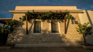 Un edificio con fachada de ladrillo, dos ventanas con contraventanas y una pérgola cubierta de hiedra.