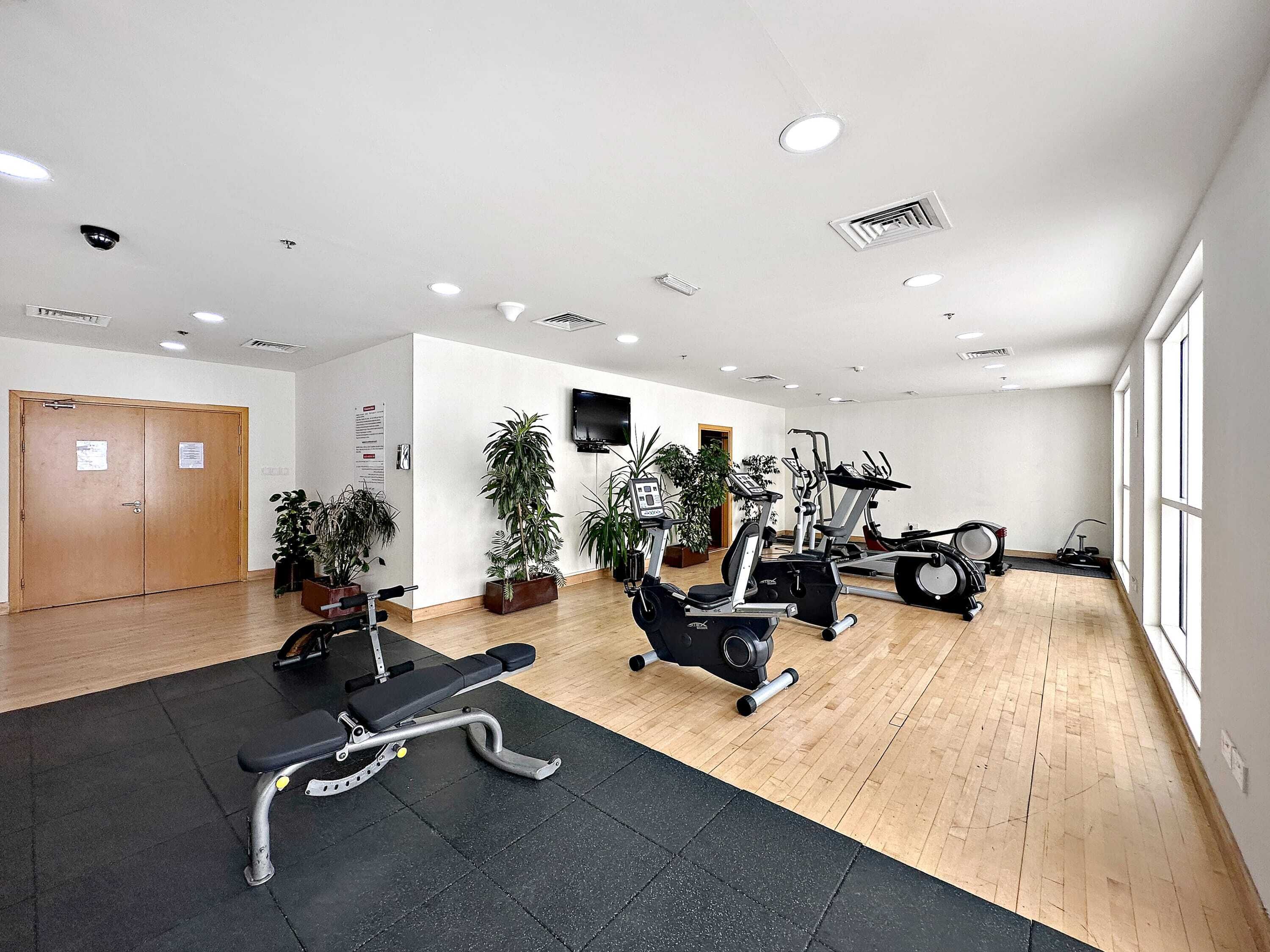 A gym with exercise equipment, wooden flooring, and large windows.