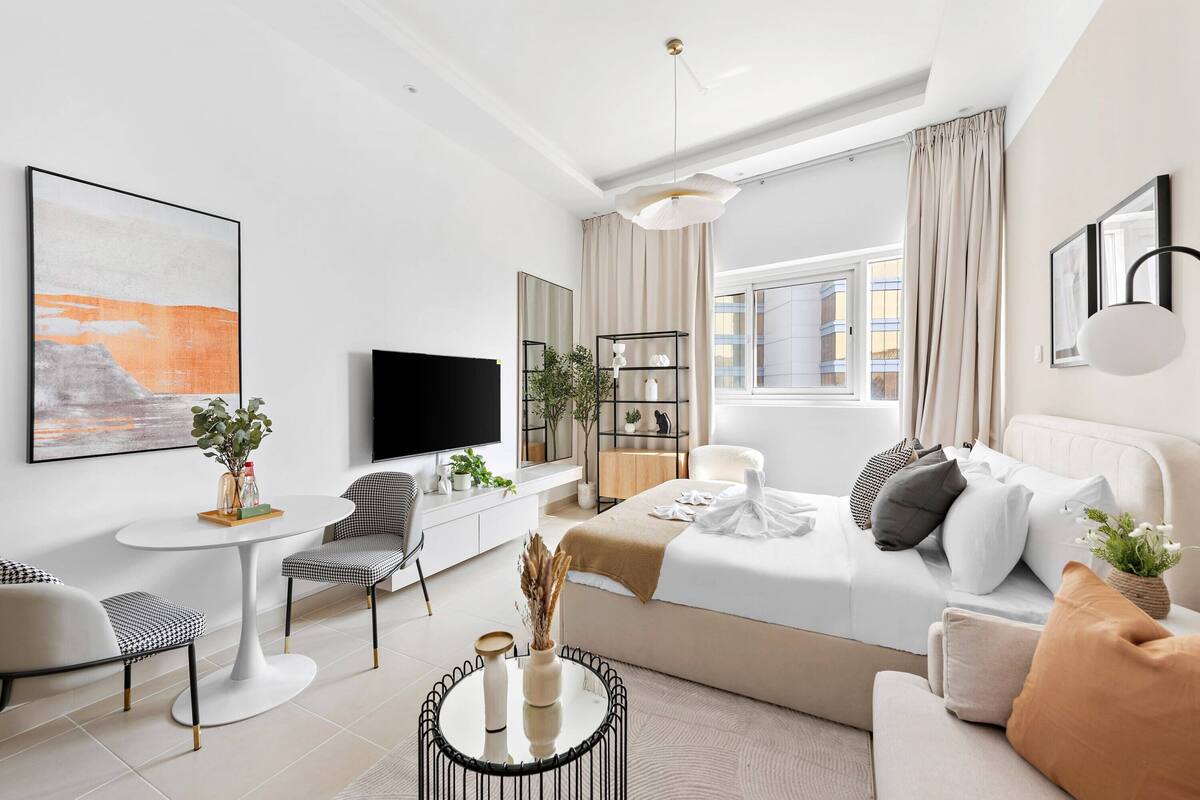 A modern hotel room with a bed, a TV, a dining table, and a sofa.
