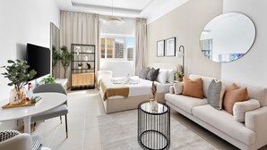 A modern hotel room with a large bed, a sitting area with a sofa and a round coffee table, a dining table with chairs, and a TV. - Silkhaus ASB Tower (Dubai)