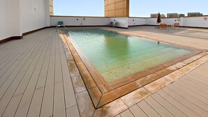 A rooftop swimming pool with a wooden deck, lounge chairs, and a view of the city skyline. - Silkhaus ASB Tower (Dubai)