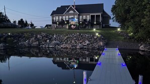Une propriété située au bord de l’eau, dotée d’un quai s’étendant dans une zone d’eau calme, d’une grande maison avec une véranda et d’un mât sur lequel flotte le drapeau américain.