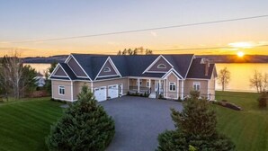 Une grande maison de plain-pied avec un garage, une allée couverte et une vue sur un lac au coucher du soleil.