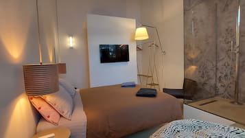 Ein Hotelzimmer mit Bett, Nachttisch, Lampe, Fernseher und Duschbereich.