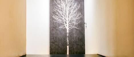 A hallway with a dark floor and a wall featuring a white tree silhouette with the text "LOFT 19" on it.