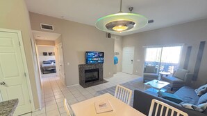 A modern living room with a fireplace, a dining area, and a TV mounted on the wall. - McDowell Mountain Adventure Condo - Quiet, Heated Pool, Close to Downtown (Fountain Hills)
