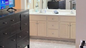 A bathroom with a wooden vanity, a large mirror, a sink, and a television displaying streaming services. - McDowell Mountain Adventure Condo - Quiet, Heated Pool, Close to Downtown (Fountain Hills)