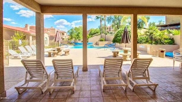 A covered outdoor area with lounge chairs, a pool, and a view of the surrounding buildings. - McDowell Mountain Adventure Condo - Quiet, Heated Pool, Close to Downtown (Fountain Hills)