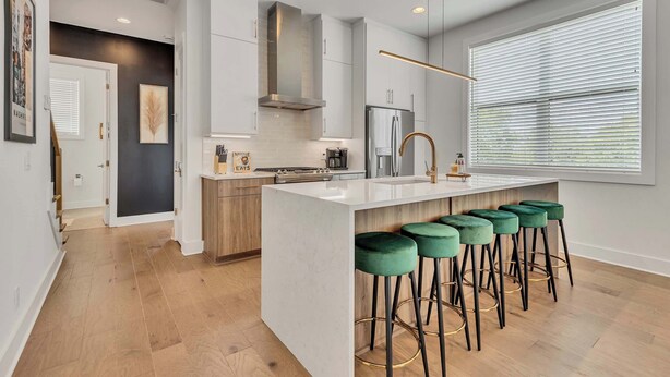 A modern kitchen with a central island, bar stools, and a large window with blinds. - 2 Luxury New Homes | Near Broadway + Rooftop Views (Nashville)