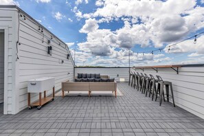 A rooftop terrace with a sofa, chairs, and a cart.