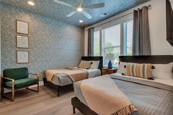 A bedroom with two beds, a green armchair, and a ceiling fan.
