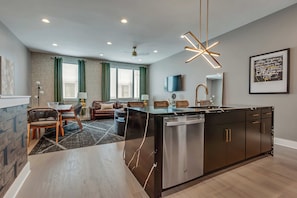 Una cocina moderna con una isla central, un área de comedor con sillas, un sofá y un televisor montado en la pared.