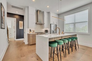 A modern kitchen with a central island, bar stools, and a large window with blinds.