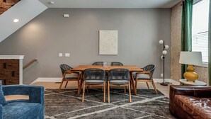 A dining area with a wooden table and chairs, a blue armchair, a patterned rug, and a lamp. - 2 Luxe Side-by-Side Downtown Homes • Skyline Views (Nashville)