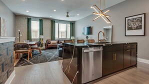 A modern kitchen with a central island, a dining area with chairs, a sofa, and a TV mounted on the wall. - 2 Luxury New Homes | Near Broadway + Rooftop Views (Nashville)