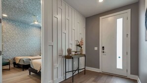 A room with a bed, a console table with decorative items, a door with a peephole, and a patterned wall. - 2 Luxury New Homes | Near Broadway + Rooftop Views (Nashville)