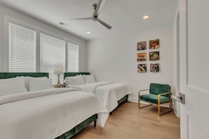 Habitación de hotel con dos camas, un ventilador de techo y una silla verde.