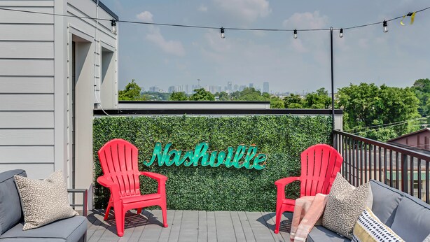 A rooftop terrace with a city skyline view, a neon sign reading "Nashville," and red Adirondack chairs. - 2 Luxe Side-by-Side Downtown Homes • Skyline Views (Nashville)