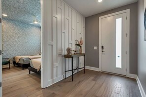 A room with a bed, a console table with decorative items, a door with a peephole, and a patterned wall.