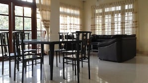 Amplia sala de estar con mesa de comedor, sillas, sofá y ventanas grandes con cortinas.