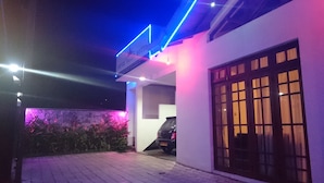 Entrada de hotel con un letrero, un coche estacionado en la entrada y un muro de piedra con plantas.