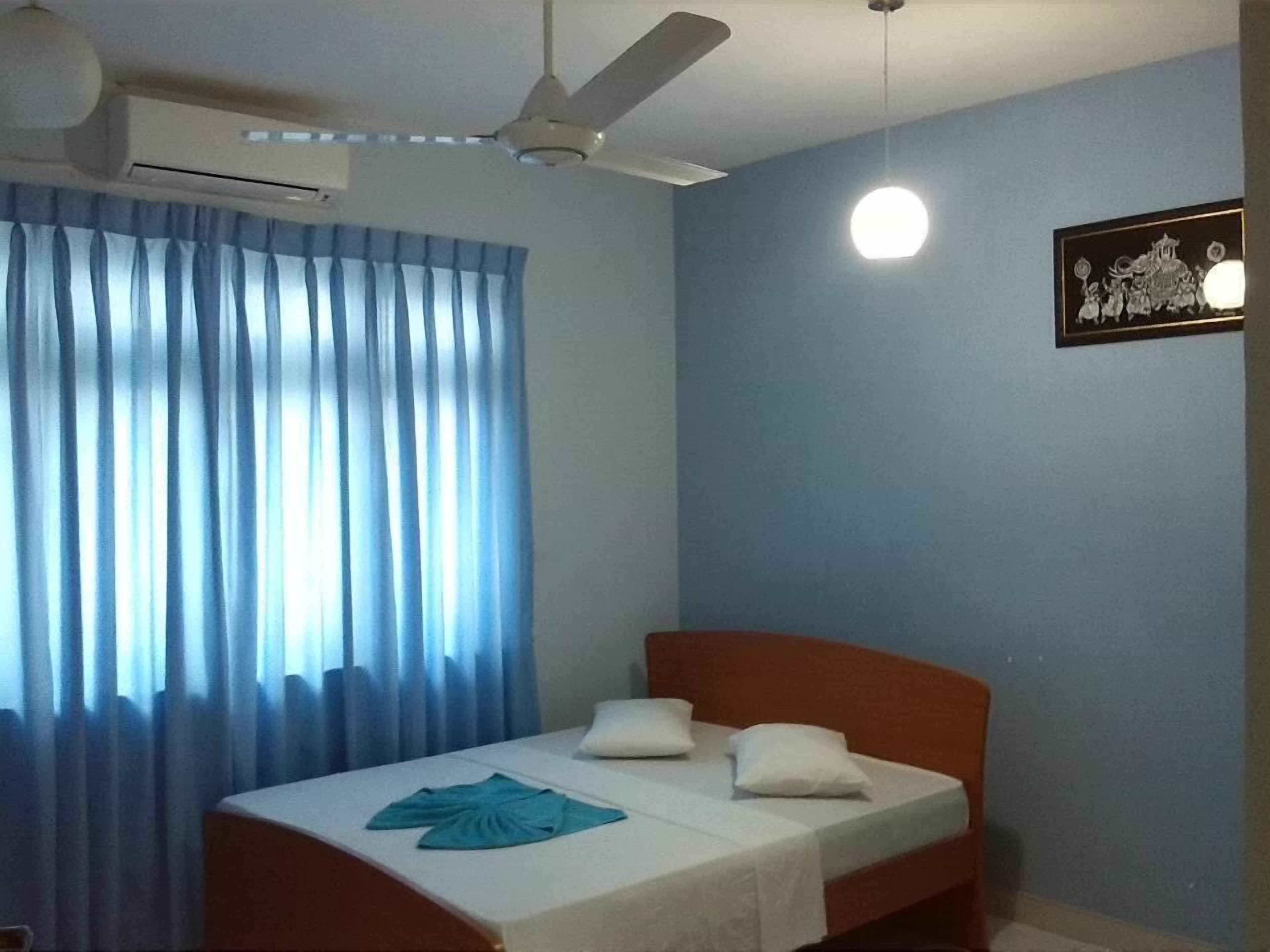 A bedroom with a bed, curtains, a ceiling fan, and a wall-mounted light fixture.