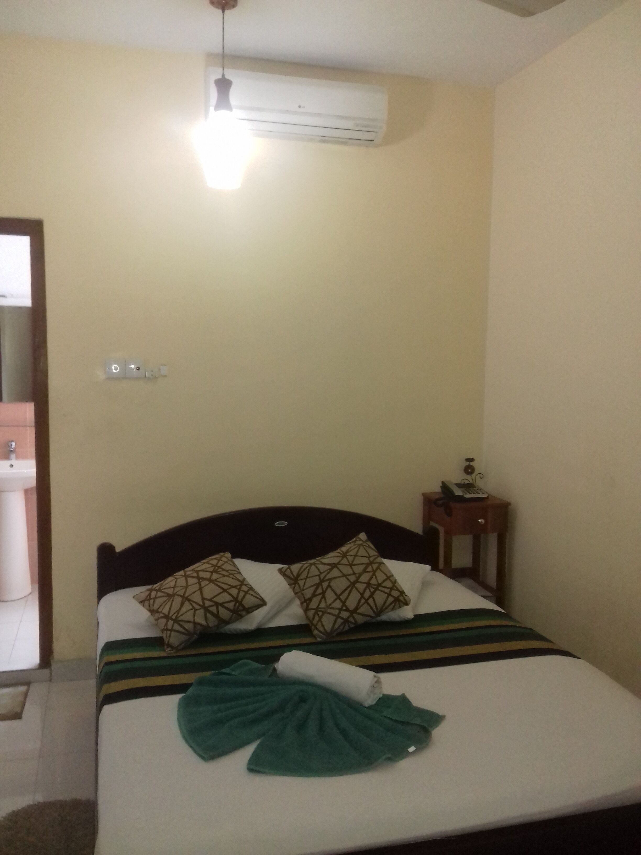 A hotel room with a bed, a bedside table with a phone, and an air conditioning unit on the wall.