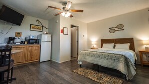 Une chambre à coucher avec un lit, un ventilateur de plafond, une table de chevet avec une lampe, une tête de lit en bois et une raquette de tennis accrochée au mur.