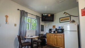 Une petite cuisine équipée d’une table et de chaises, d’un réfrigérateur, d’un four à micro-ondes et d’un téléviseur.