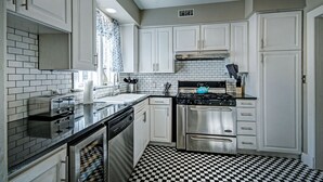 Une cuisine avec des meubles blancs, un carrelage noir et blanc, une cuisinière en acier inoxydable et un lave-vaisselle.