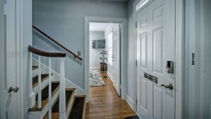 Un couloir avec un escalier en bois, des portes blanches et un tapis sur le sol.