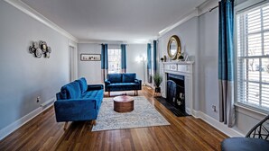 Un salon avec une cheminée, deux canapés bleus, une table basse et une grande fenêtre avec des rideaux.