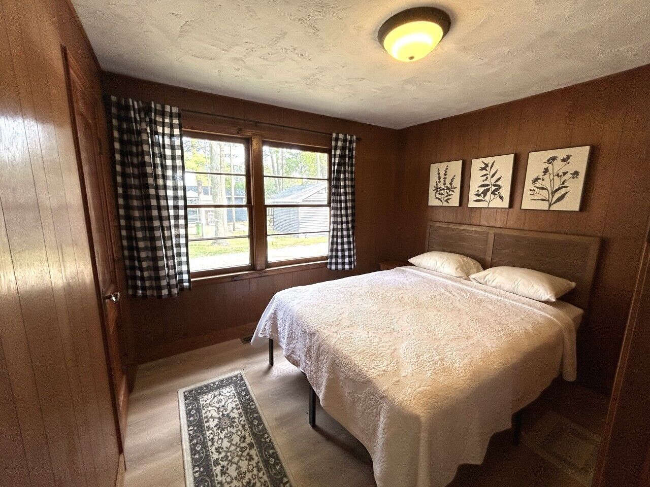 A bedroom with a bed, a window with curtains, and wall art.
