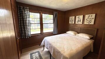 A bedroom with a bed, a window with curtains, and wall art.