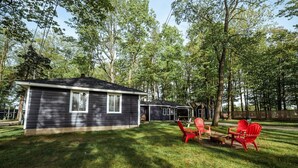 Une cabane à deux étages, à l’extérieur sombre, entourée d’une cour verdoyante et d’arbres.