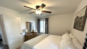 Une chambre à coucher comprenant un lit, un ventilateur de plafond, une commode, une fenêtre avec des rideaux et une porte.