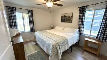 A bedroom with a bed, a ceiling fan, a window with curtains, a bedside table, and a rug.