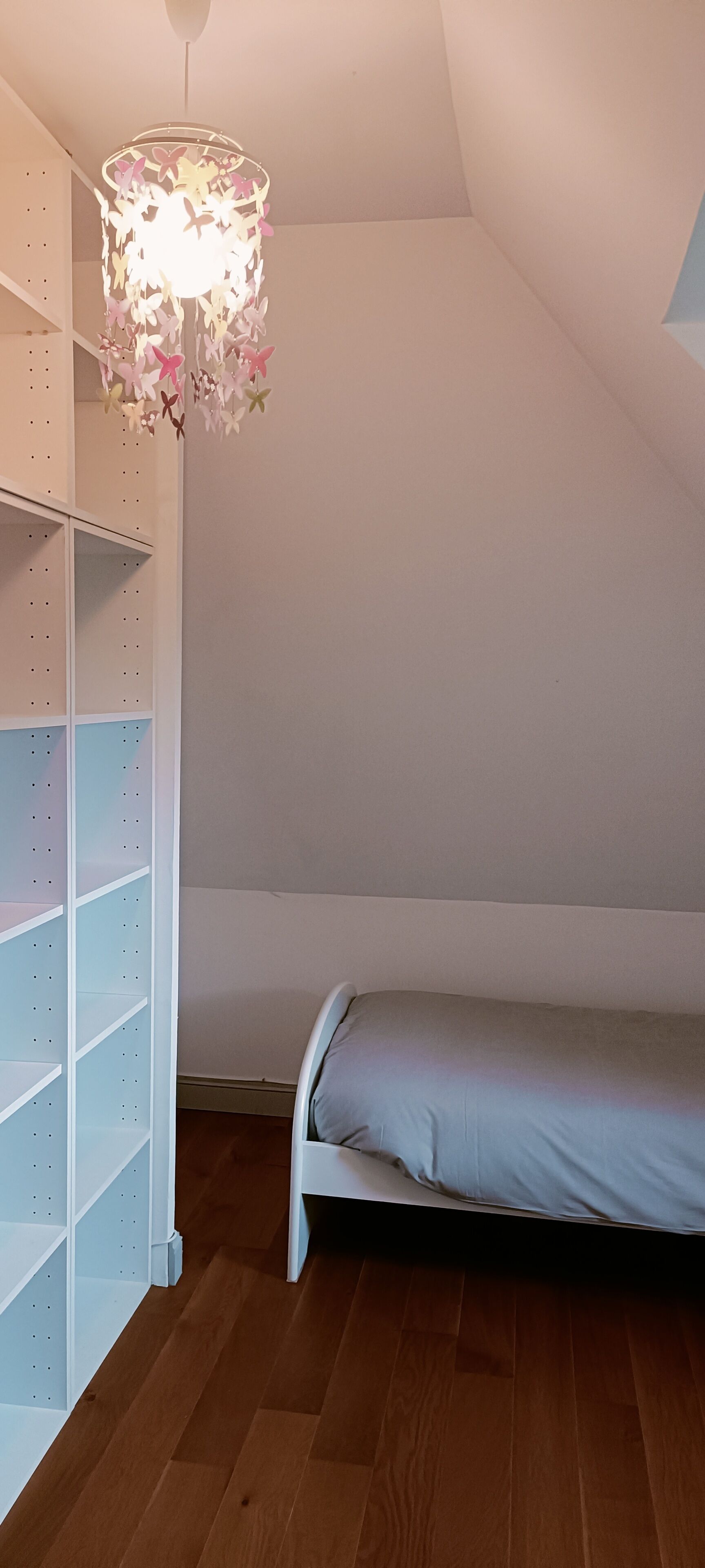 A bedroom with a bed, a white shelving unit, and a hanging light fixture.
