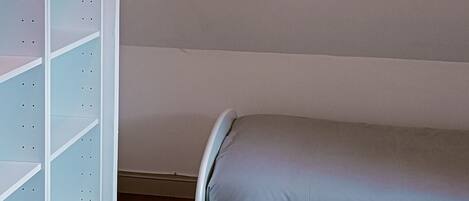 A bedroom with a bed, a white shelving unit, and a hanging light fixture.